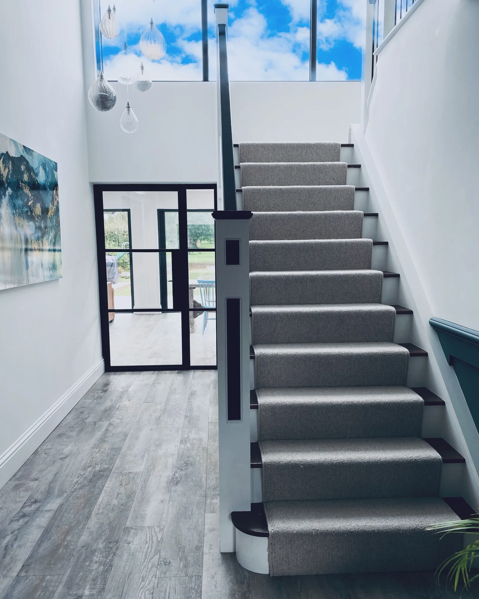 A grey carpeted staircase beside black framed glazing in the hallway