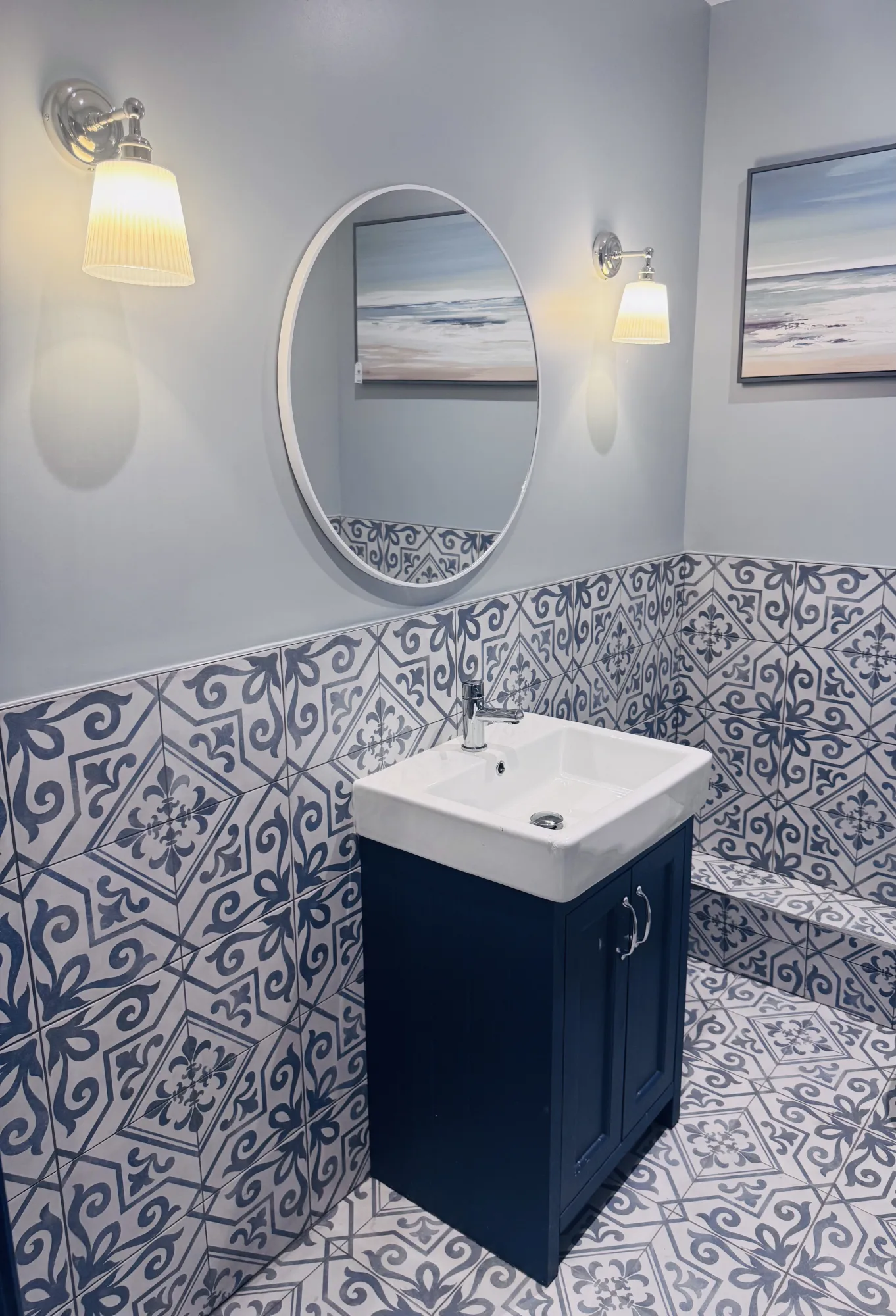 Rest room with a navy vanity unit, round mirror and blue and white patterned tiling, Amalfi Bar & Cafe, Bideford, Devon