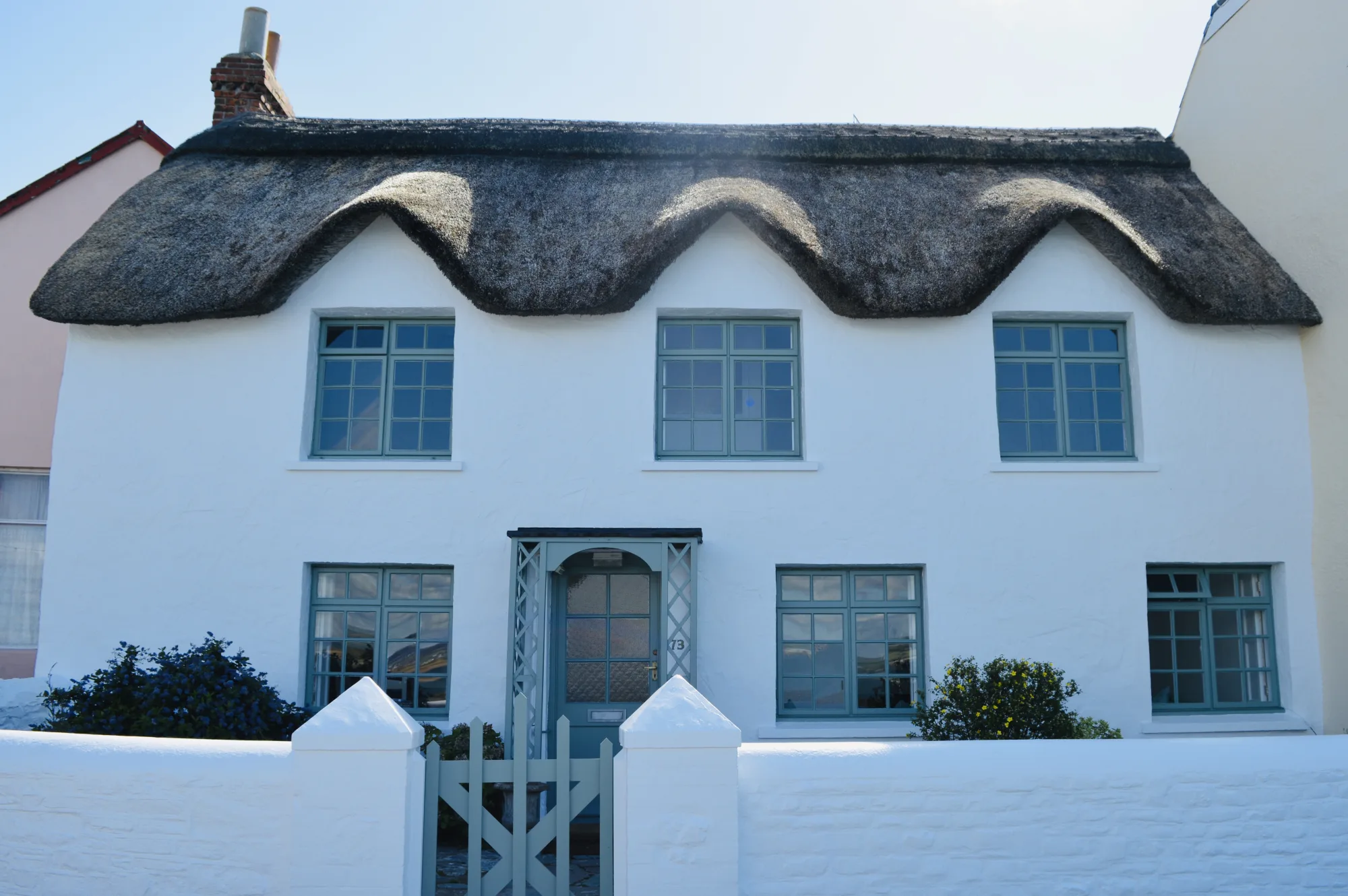 The whitewashed front of the 18th century thatched cottage in Appledore, Devon, with sage green sash windows and a matching gated porch