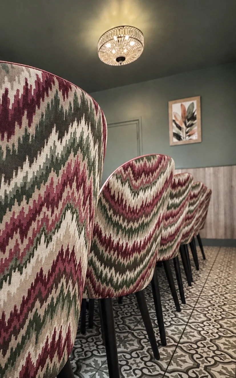 Bespoke flamestitch dining chairs lined along the function room table beneath a crystal flush chandelier, Belluno Restaurant, Bideford, Devon