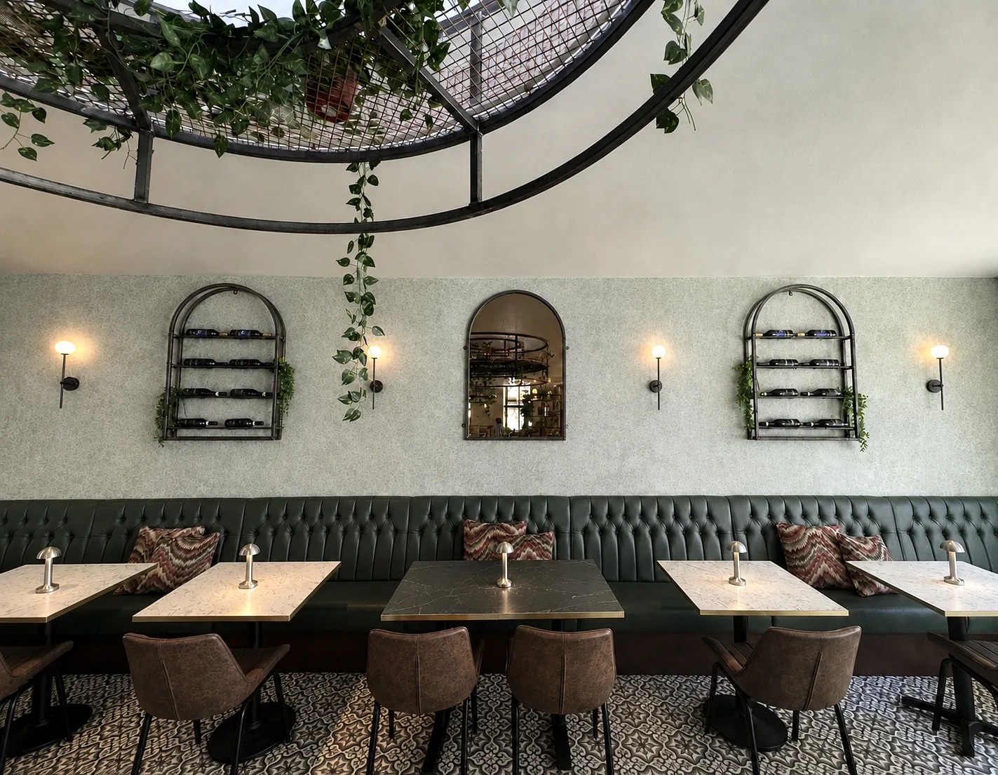 Back seating area with arched wine racks, a mirror and trailing plants above the banquette, Belluno Restaurant, Bideford, Devon
