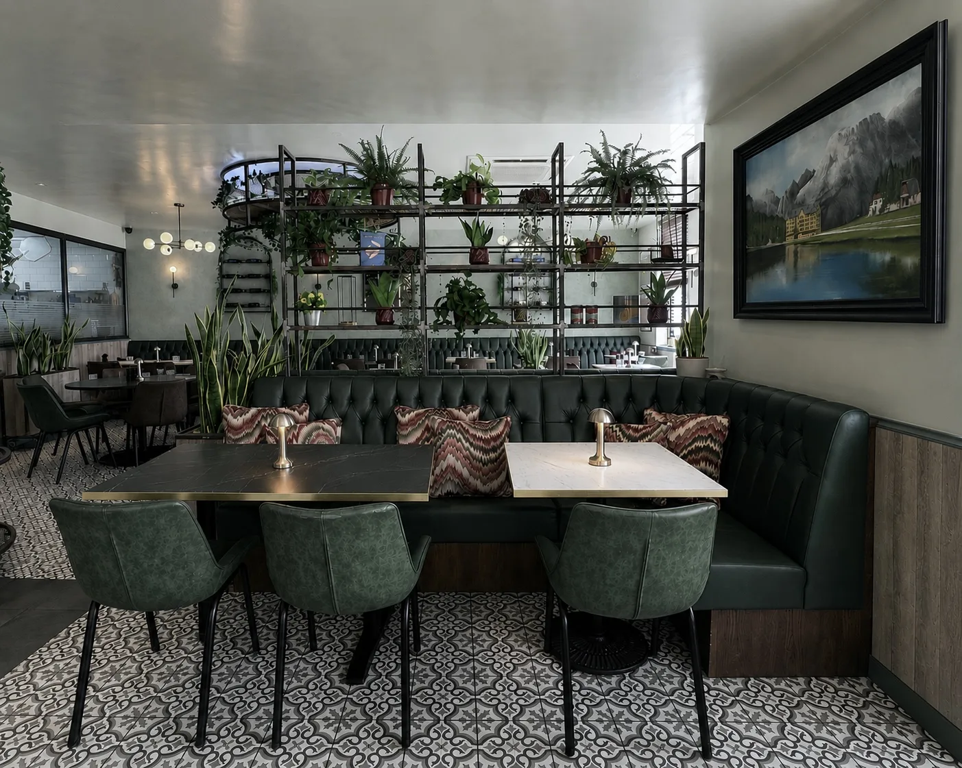 Green button backed corner banquette below plant shelving, with patterned floor tiles, at Belluno Restaurant in Bideford, Devon