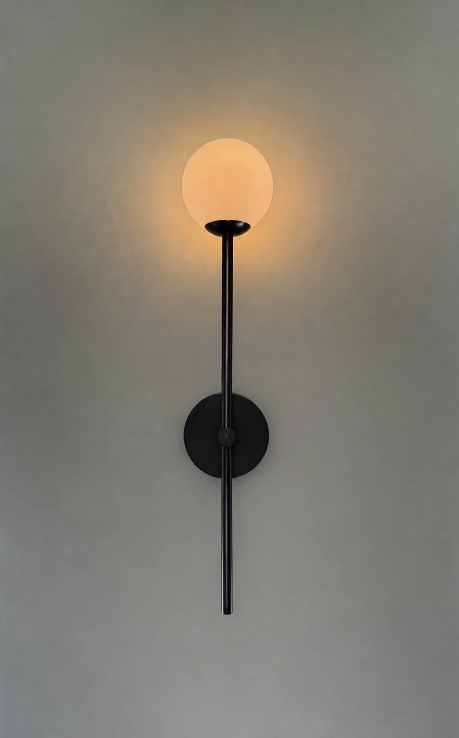 Slim black wall light with an opal glass globe against a soft grey wall, Belluno Restaurant, Bideford, Devon