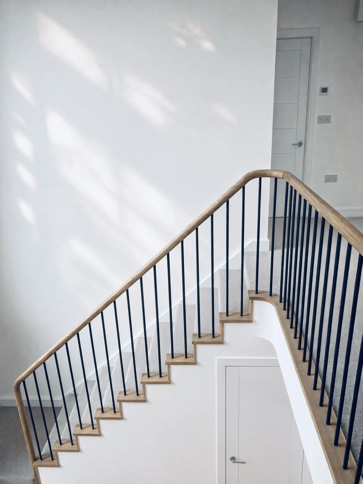 Bespoke staircase with an oak hand rail and slender black metal spindles, in a contemporary new build in Northam, Devon