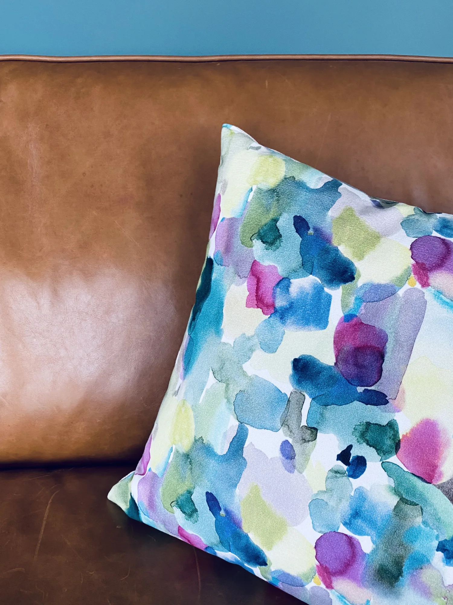 Tan leather Timothy Oulton sofa with a Bluebell Gray watercolour cushion against a teal wall, Northam, Devon