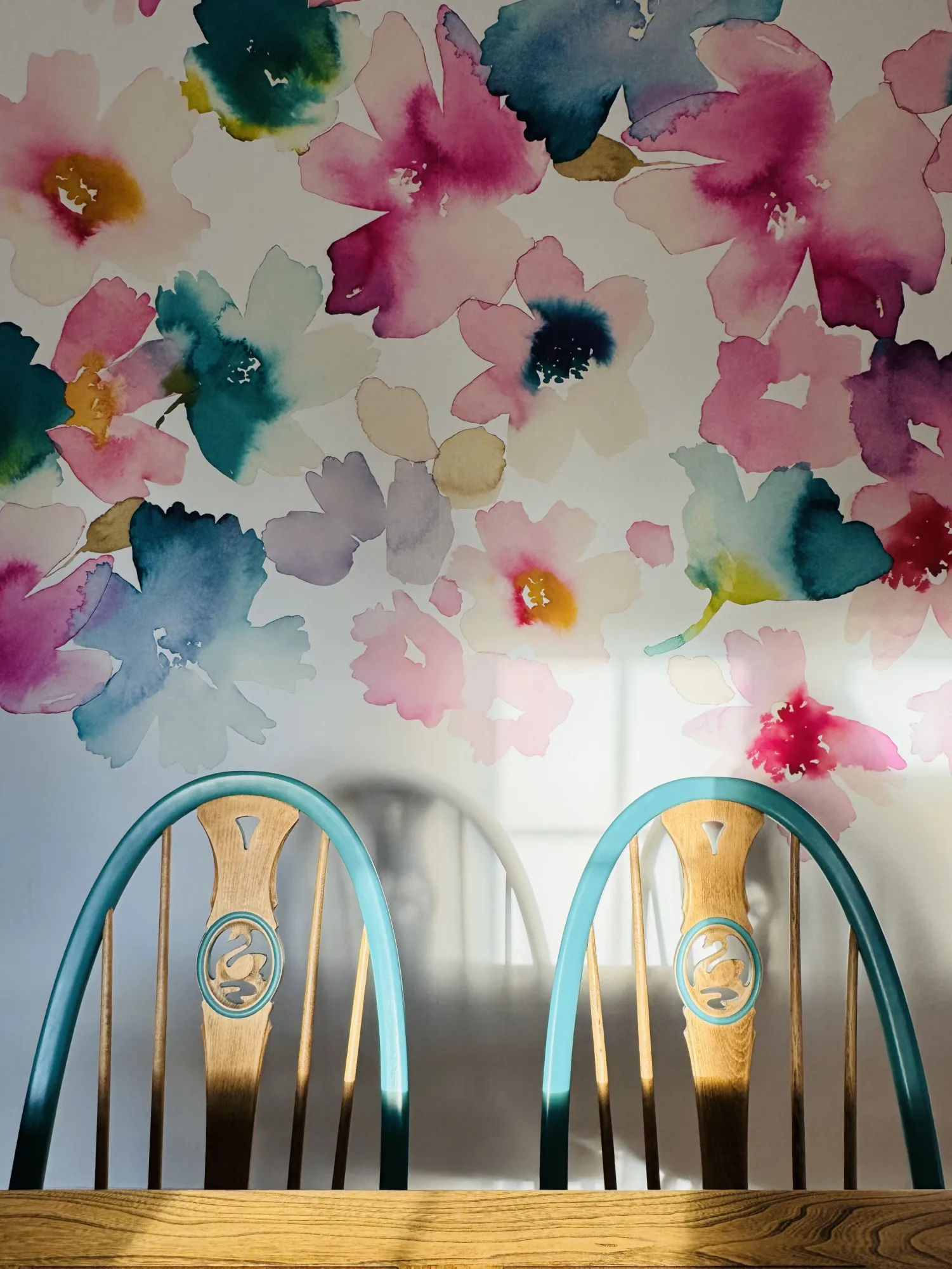 Upcycled Ercol chairs in oak and teal below a Bluebell Gray Sanna floral mural, at a converted stable block cottage in Stevenstone, Devon