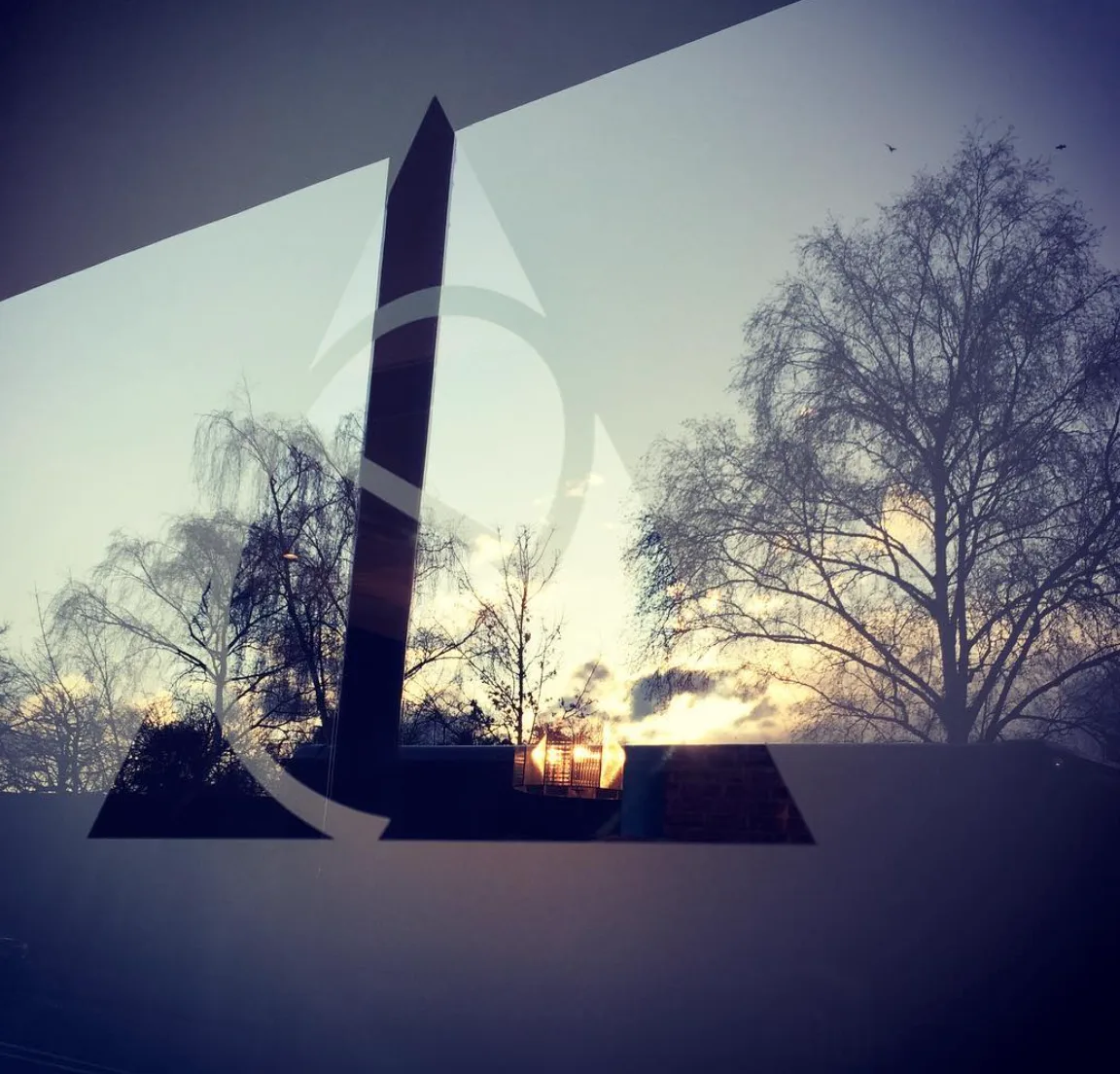 The Ethos mark etched into the glass of the front door, with bare trees and a low sun behind it, at Ethos HQ in London