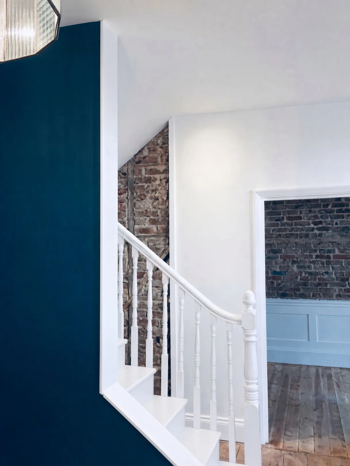 Hallway in deep teal with white joinery and exposed brick beyond, Ethos HQ, London