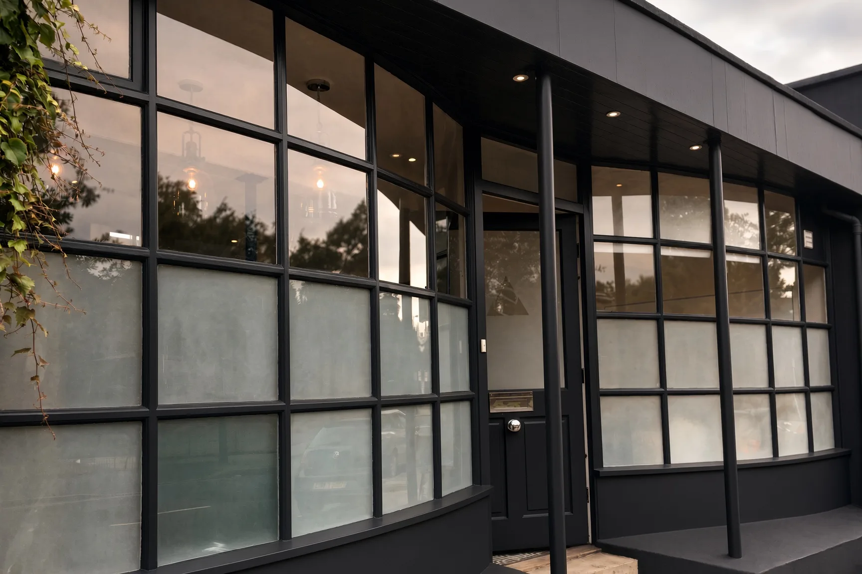 The Ethos HQ frontage in black framed Crittall style glazing, with a black front door and climbing greenery, London