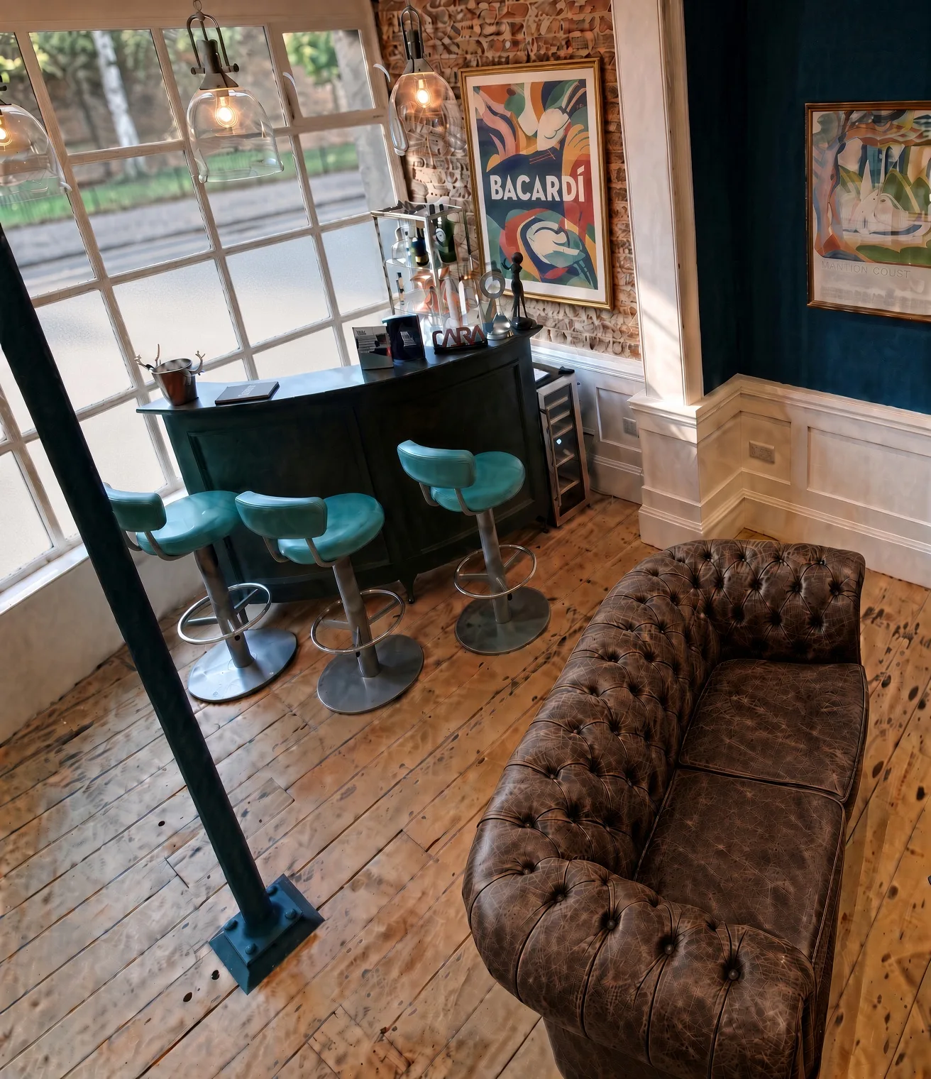Reception bar in dark green with teal bar stools and a brown leather Chesterfield, against exposed brick, Ethos HQ, London