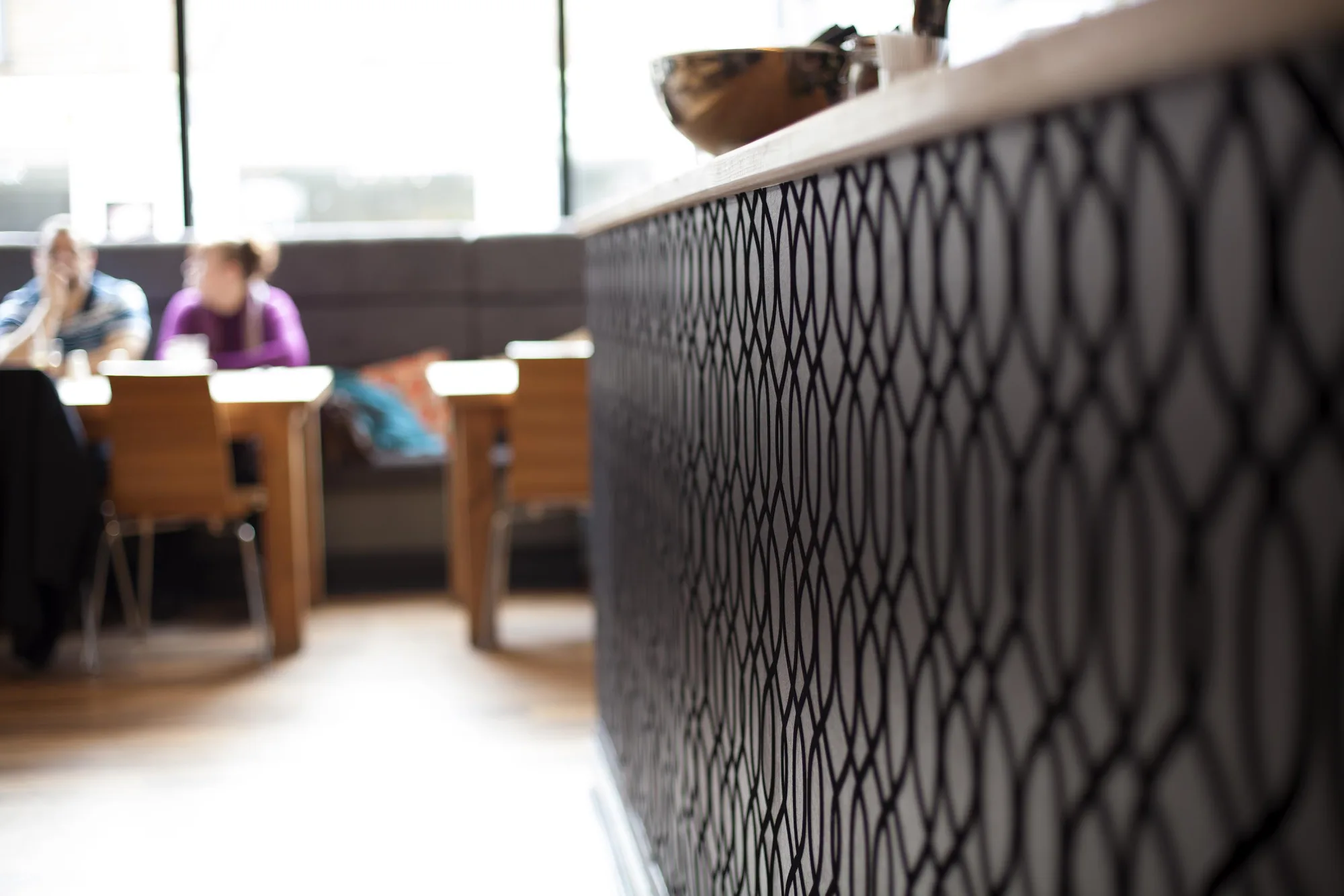 Bar counter fronted in black geometric flock wallpaper, with the window seating behind, at Swell Bar & Kitchen in Truro, Cornwall