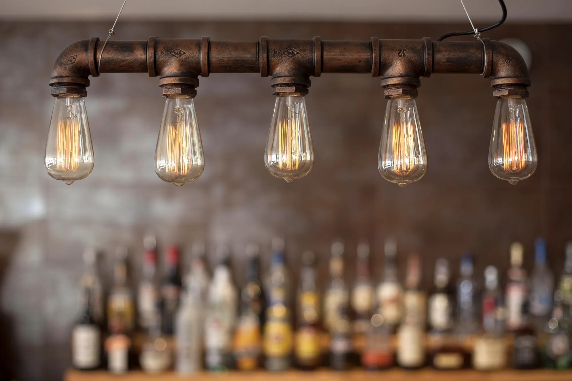 Copper pipe pendant with five exposed filament bulbs lit above the back bar bottles, at Swell Bar & Kitchen in Truro, Cornwall