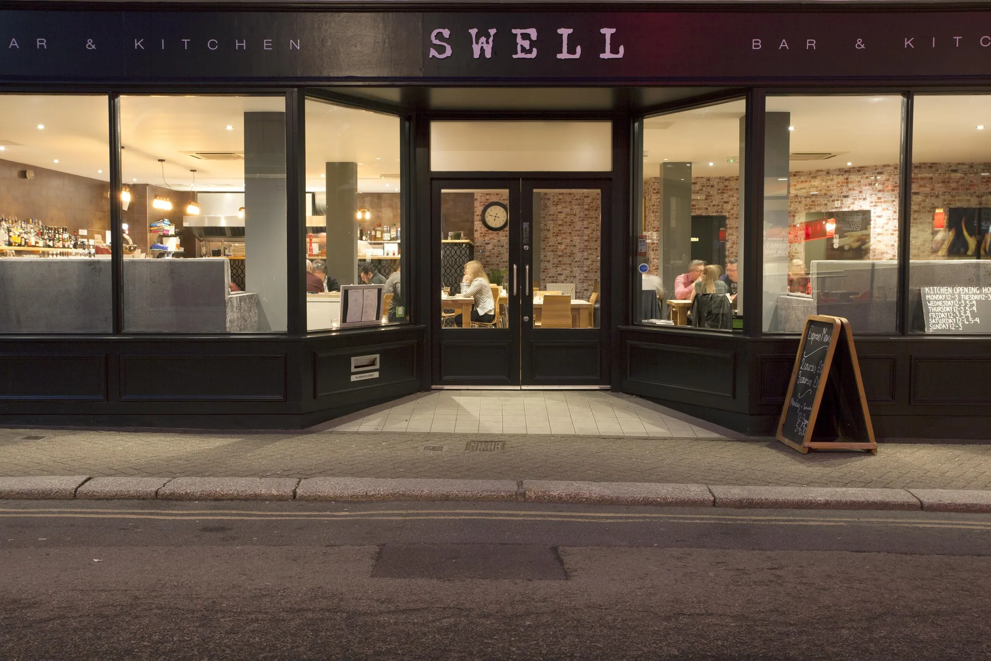 The shopfront lit at night, in black timber with gold lettering, at Swell Bar & Kitchen in Truro, Cornwall
