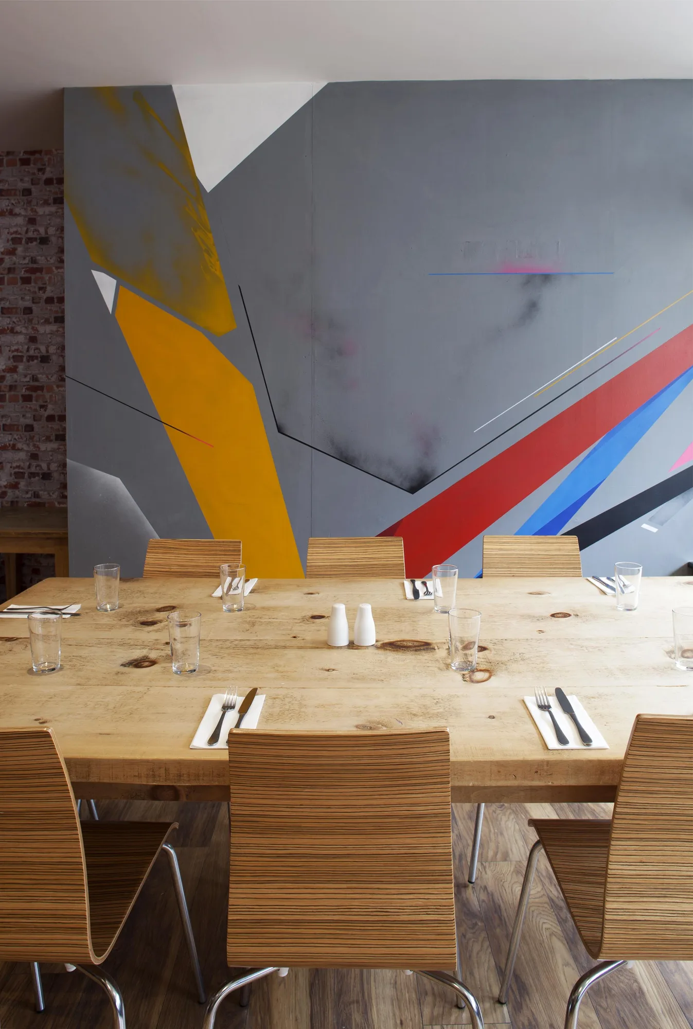 Long reclaimed timber table laid for dinner in front of the geometric wall mural, at Swell Bar & Kitchen in Truro, Cornwall