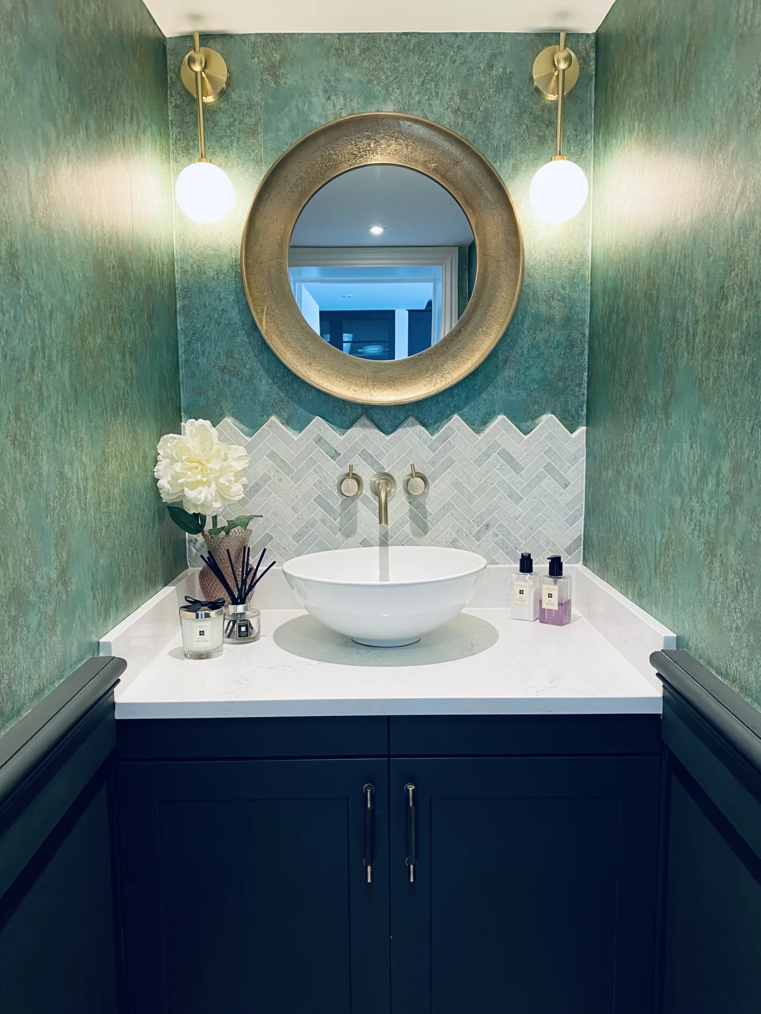 Downstairs cloakroom with green textured walls, a round gold mirror and herringbone marble tiling, Topsham, Devon