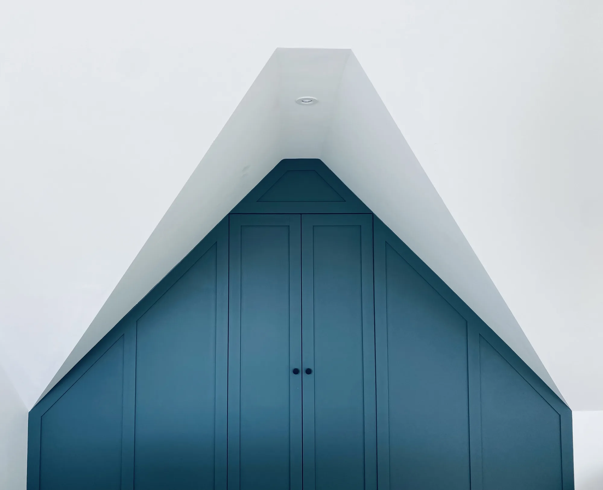 Bespoke teal wardrobes built into the eaves apex, with the ceiling sloping to a point above them, at an art deco house in Topsham, Devon