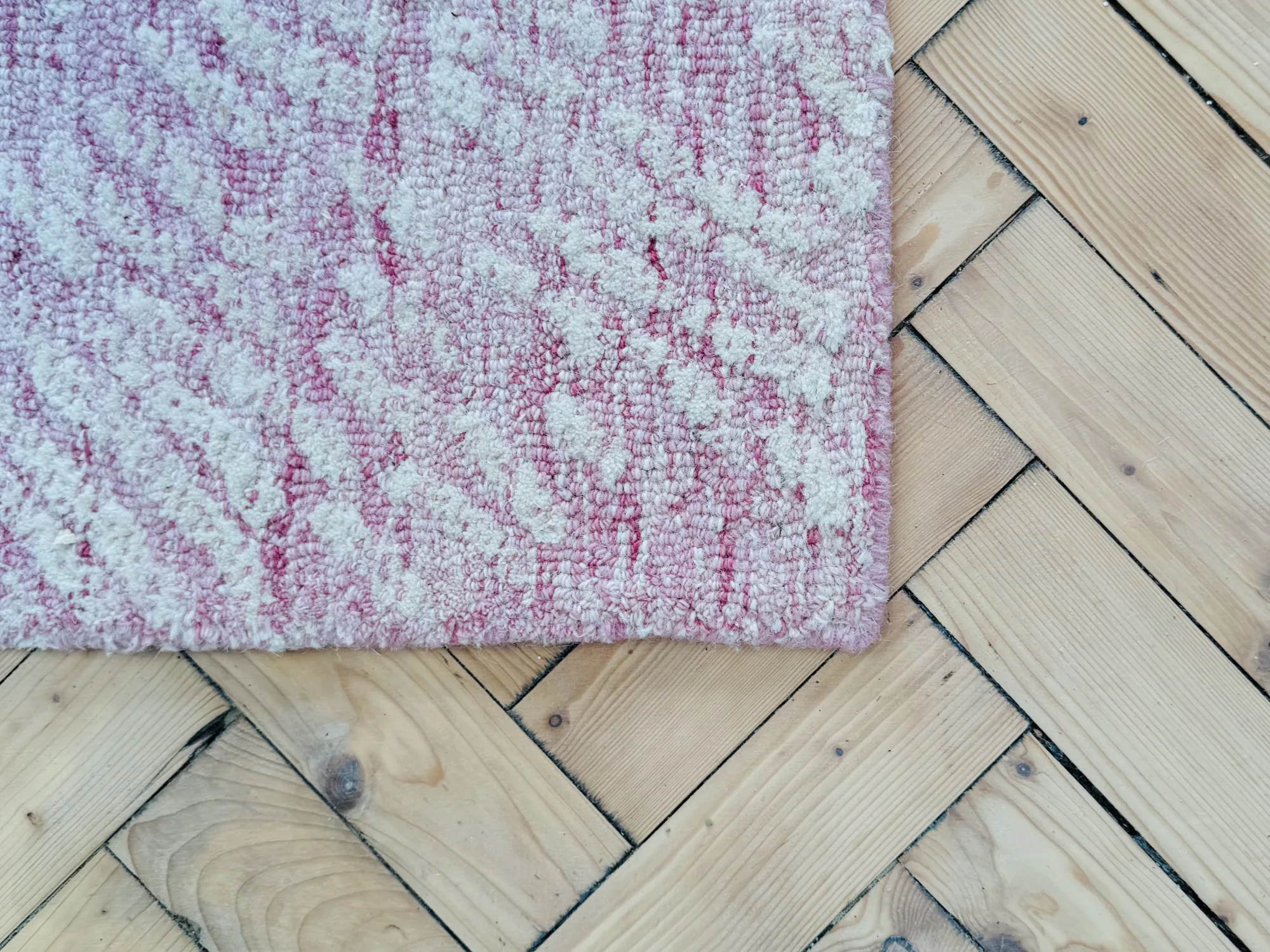 Restored original parquet flooring with the corner of a pink wool rug, at the converted stable block in Stevenstone, Devon